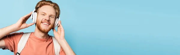 Conceito panorâmico de estudante de barba e ruiva tocando fones de ouvido sem fio em azul — Fotografia de Stock