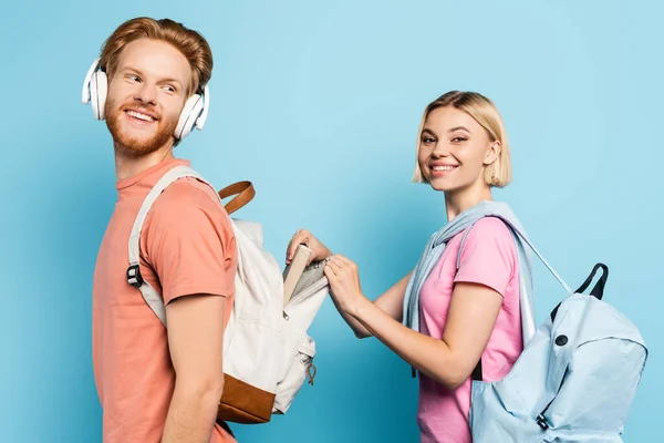 Blonde Studentin berührt Rucksack eines bärtigen Freundes auf blau — Stockfoto