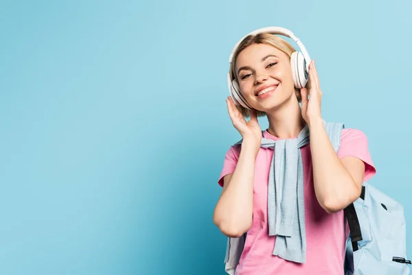 Блондинка слухає музику в бездротових навушниках на синьому — стокове фото