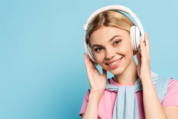 Mujer rubia escuchando música en auriculares inalámbricos en azul - foto de stock