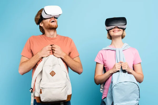 Estudantes em fones de ouvido de realidade virtual segurando mochilas em azul — Fotografia de Stock