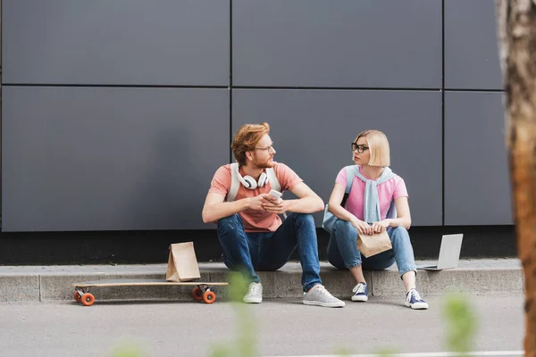 Messa a fuoco selettiva di studenti in occhiali seduti vicino skateboard e gadget mentre si guardano fuori — Foto stock