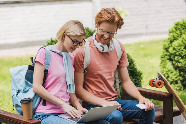 Studenti in occhiali guardando il computer portatile mentre seduti sulla panchina — Foto stock