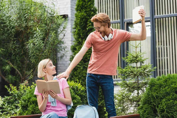 Excité rousse étudiant toucher blonde ami avec livre — Stock Photo