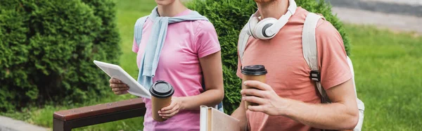 Panoramic crop of young students holding paper cups, digital tablet and books outside — Stock Photo