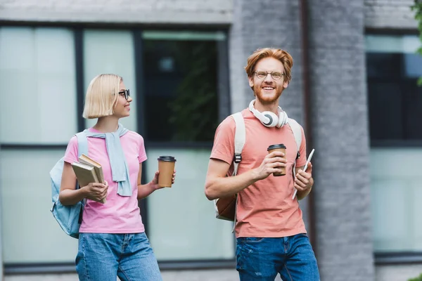 Jóvenes estudiantes sosteniendo café para llevar, tableta digital y libros fuera - foto de stock