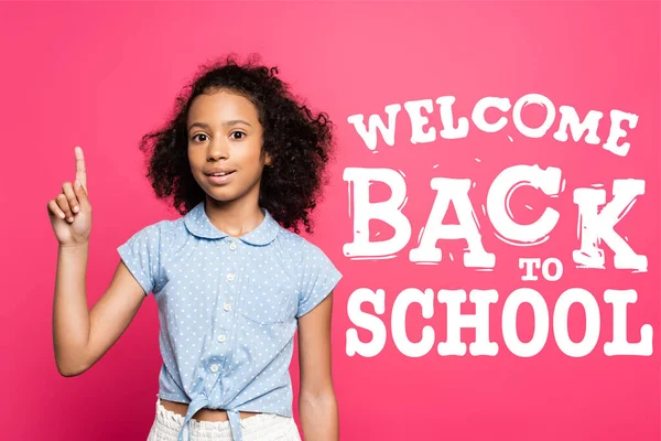 Curly african american kid showing idea gesture near welcome back to school lettering on pink — Stock Photo