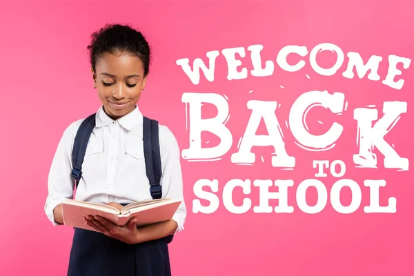 African american schoolgirl reading book near welcome back to school lettering on pink — Stock Photo