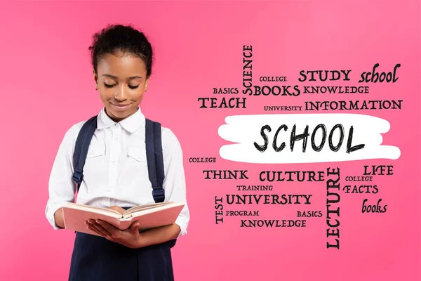 Colegiala afroamericana leyendo libro cerca de la escuela letras en rosa - foto de stock