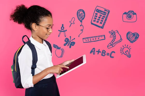 Afro-américaine écolière dans des lunettes avec sac à dos en utilisant une tablette numérique près abc lettrage et illustration sur rose — Photo de stock