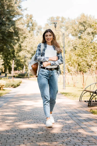Frau im karierten Hemd hält Laptop in der Hand und blickt beim Spazierengehen im Park in die Kamera — Stockfoto