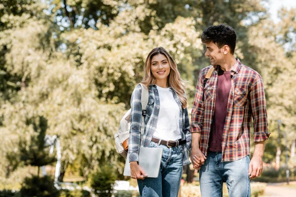 Woman with laptop holding hands with man in park — Stock Photo