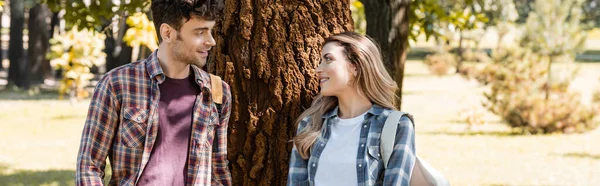 Panoramic concept of man and woman looking at each other near tree trunk — Stock Photo