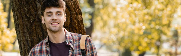 Panoramic orientation of man in checkered shirt looking at camera near tree trunk — Stock Photo