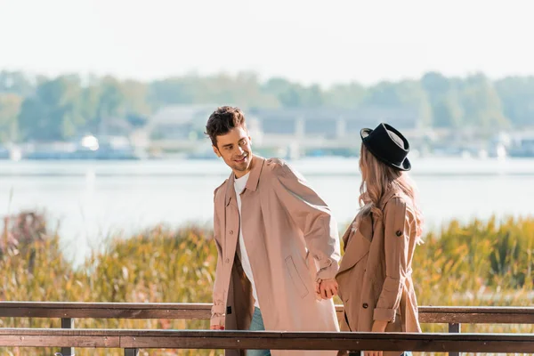 Homme en trench coat tenant la main avec femme en chapeau — Photo de stock