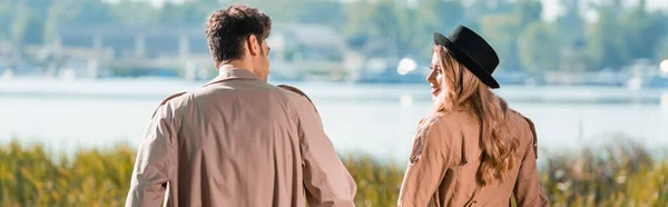 Panoramic concept of couple in trench coats looking at each other — Stock Photo