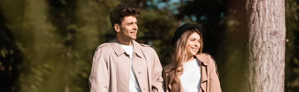 Panoramic shot of couple in trench coats looking away in park — Stock Photo