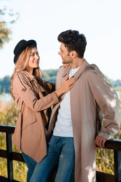 Mujer en sombrero y gabardina tocando novio en parque otoñal - foto de stock