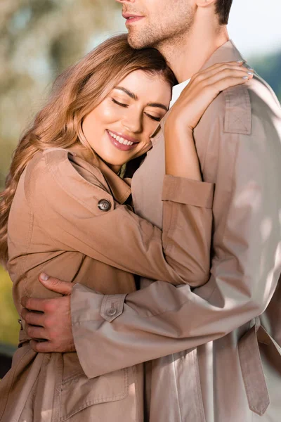 Mujer con los ojos cerrados abrazando hombre en gabardina - foto de stock