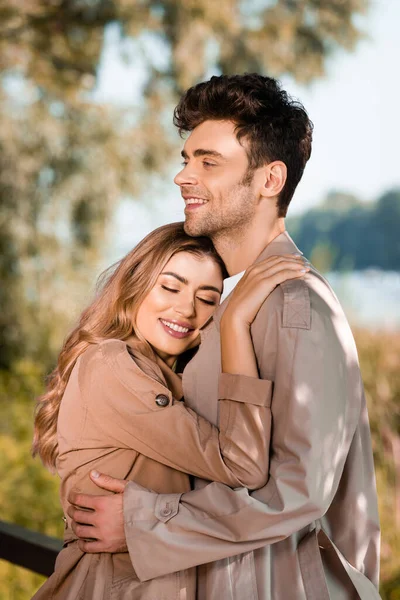 Mujer con los ojos cerrados abrazando hombre en gabardina exterior - foto de stock