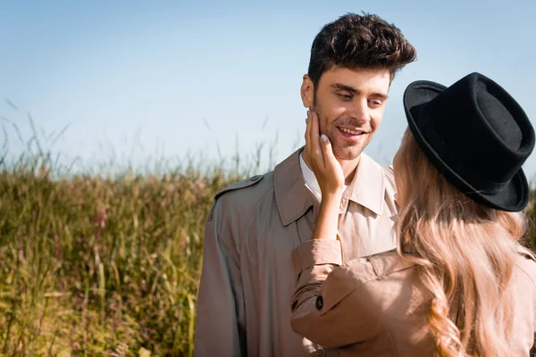 Blonde woman in hat touching face of man in trench coat — Stock Photo