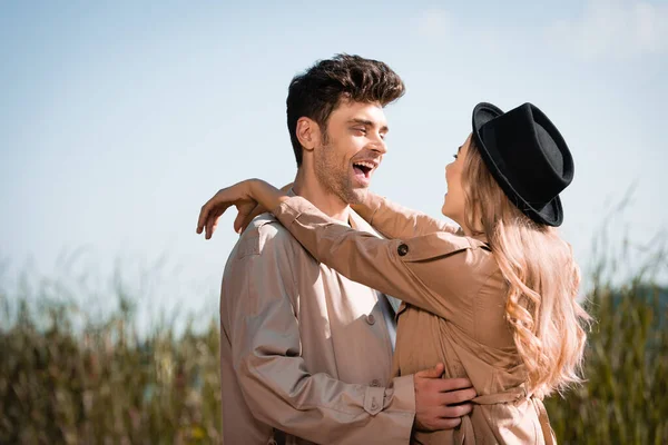 Femme blonde en chapeau étreignant homme excité en trench coat — Photo de stock