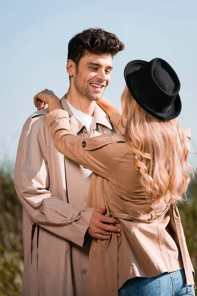 Blonde woman in black hat hugging man in trench coat — Stock Photo