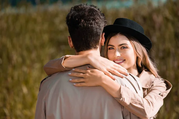 Blonde woman in black hat hugging man in trench coat — Stock Photo