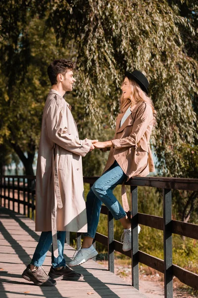 Perfil de homem e mulher em casacos de trincheira olhando uns para os outros na ponte no parque outonal — Fotografia de Stock