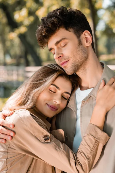 Novia abrazando novio con los ojos cerrados en el parque otoñal - foto de stock