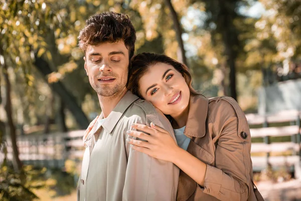 Woman looking at camera and hugging boyfriend in autumnal park — Stock Photo