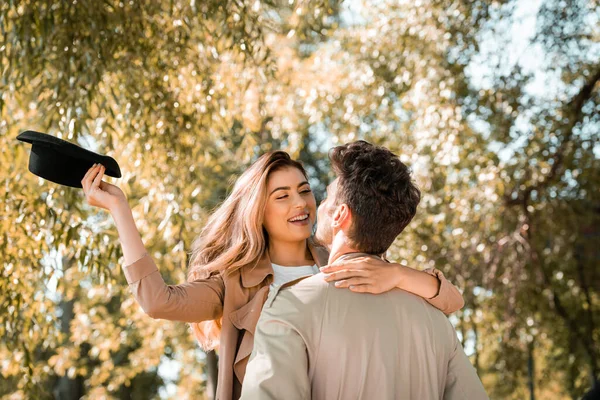 Excited woman with hat hugging boyfriend in autumnal park — Stock Photo