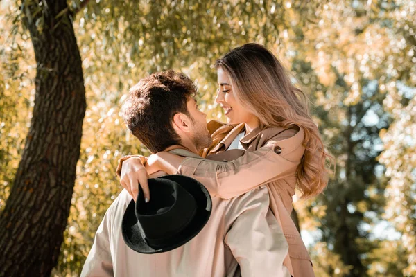 Mujer excitada con sombrero abrazando y mirando novio en el parque otoñal - foto de stock