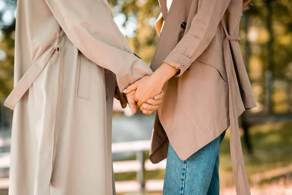 Частковий вид чоловіка і жінки в траншеї пальто тримає руки в парку — стокове фото