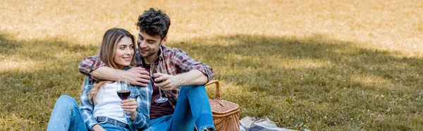 Imagen horizontal del hombre y la mujer sosteniendo vasos con vino tinto durante el picnic - foto de stock