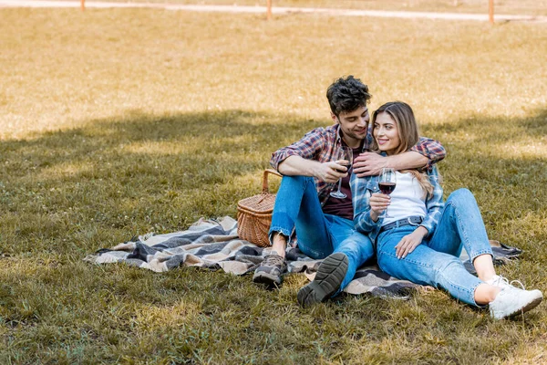 Uomo e donna seduti sulla coperta e con in mano bicchieri di vino rosso — Foto stock