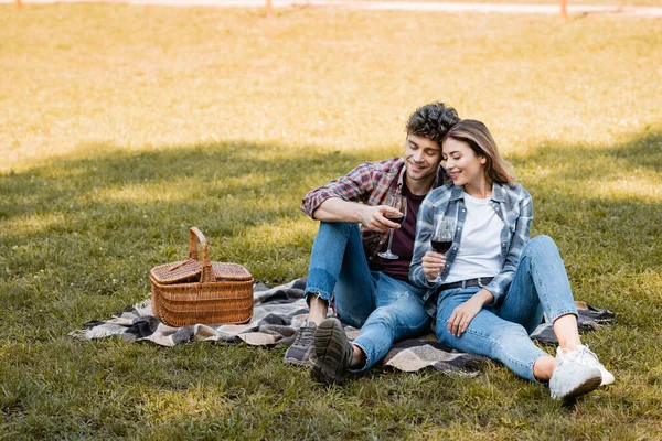 Couple sitting on plaid blanket and holding glasses of red wine — Stock Photo