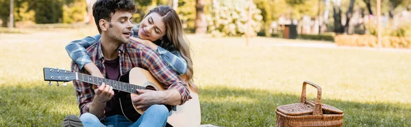Panoramic shot of woman sitting on plaid blanket and touching boyfriend playing acoustic guitar — Stock Photo