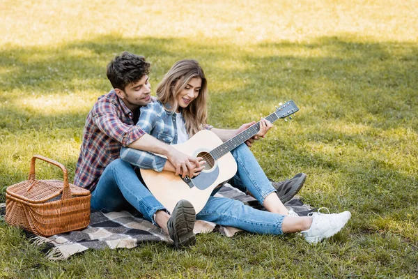 Femme assise sur une couverture à carreaux et jouant de la guitare acoustique avec son petit ami — Photo de stock