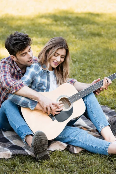 Femme assise sur une couverture et jouant de la guitare acoustique avec son petit ami — Photo de stock