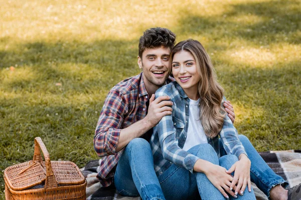 Mann und Frau sitzen neben Weidenkorb im Park — Stockfoto