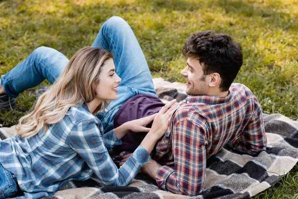 Woman lying on plaid blanket and touching boyfriend in park — Stock Photo