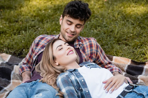 Mann sieht Frau im karierten Hemd auf Decke liegend an — Stockfoto