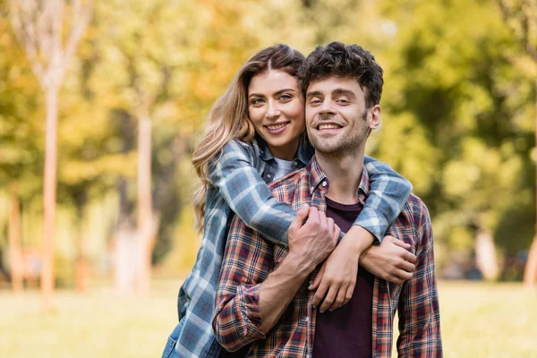 Femme embrassant l'homme en chemise à carreaux dans le parc — Photo de stock