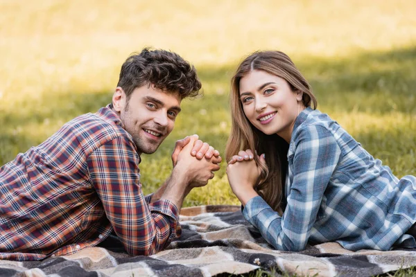 Hombre y mujer con las manos apretadas acostados sobre una manta en el parque — Stock Photo