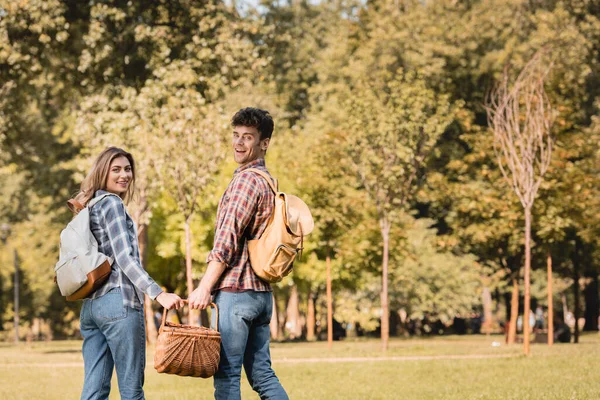 Man with wicker basket holding hands with woman while standing in park — Stock Photo