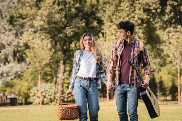 Femme avec panier en osier et homme avec guitare acoustique tenant la main dans le parc — Photo de stock