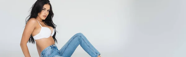 Panoramic crop of sexy and brunette woman in jeans and bra isolated on grey — Stock Photo