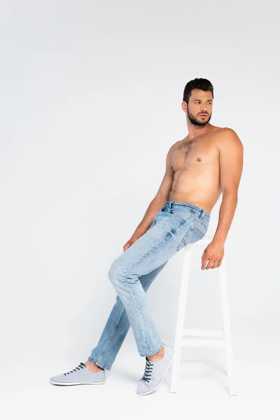 Muscular man leaning on chair and looking away on white — Stock Photo