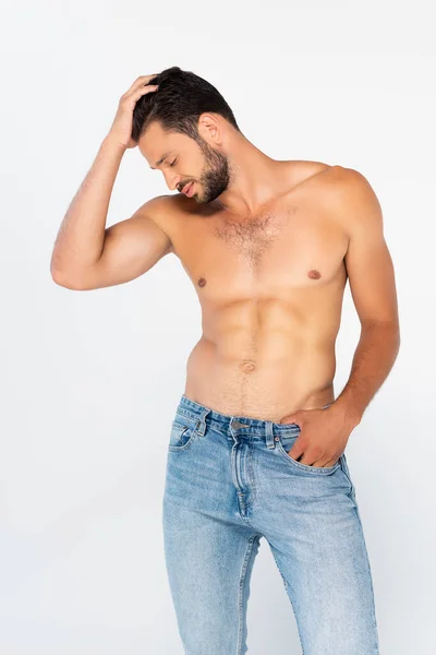 Hemdloser Mann in Jeans, der mit der Hand in der Tasche steht und die Haare isoliert auf weißem Grund berührt — Stockfoto